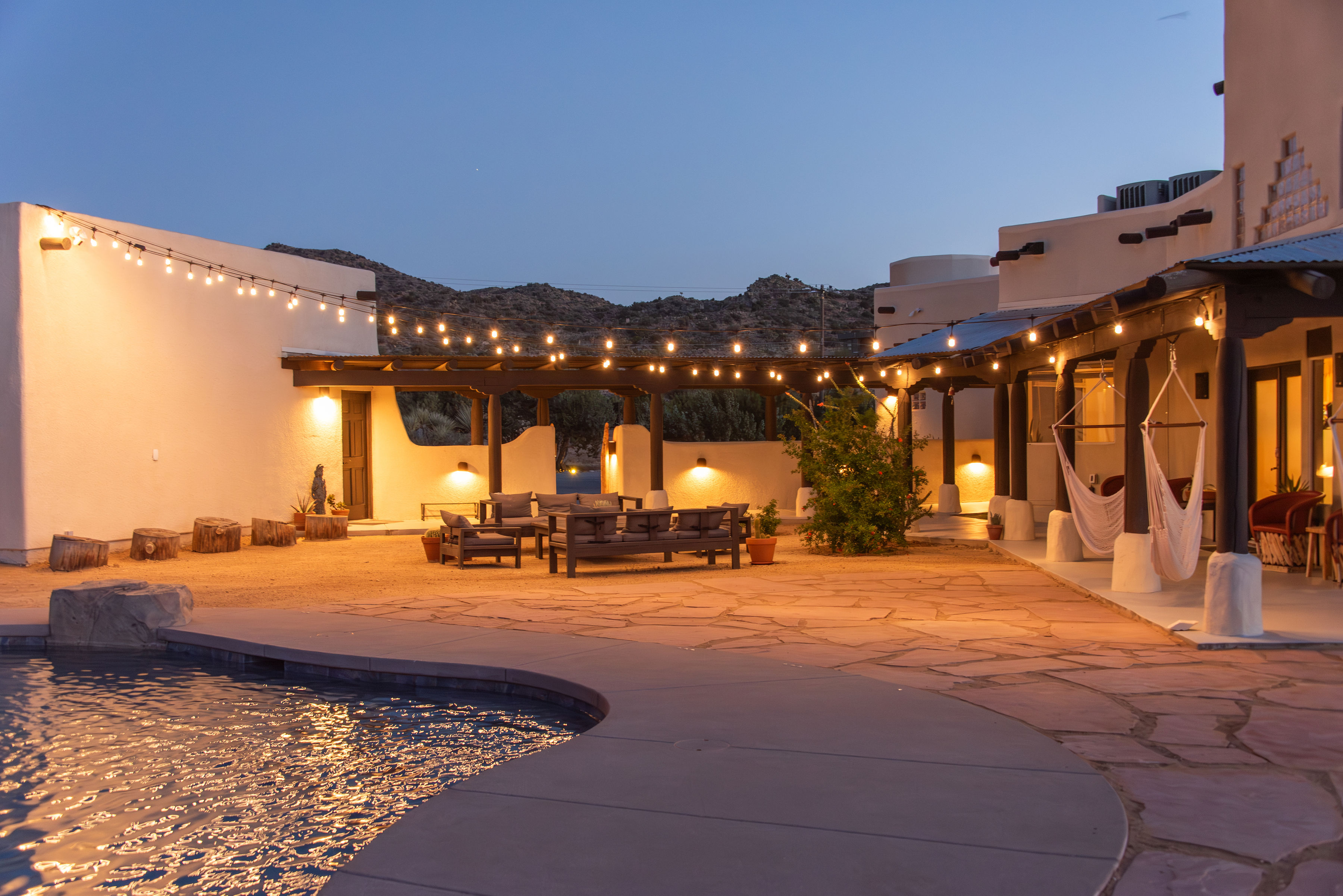 Backyard courtyard at Gaia Villa at dusk with string lights, pool, and hammock chairs