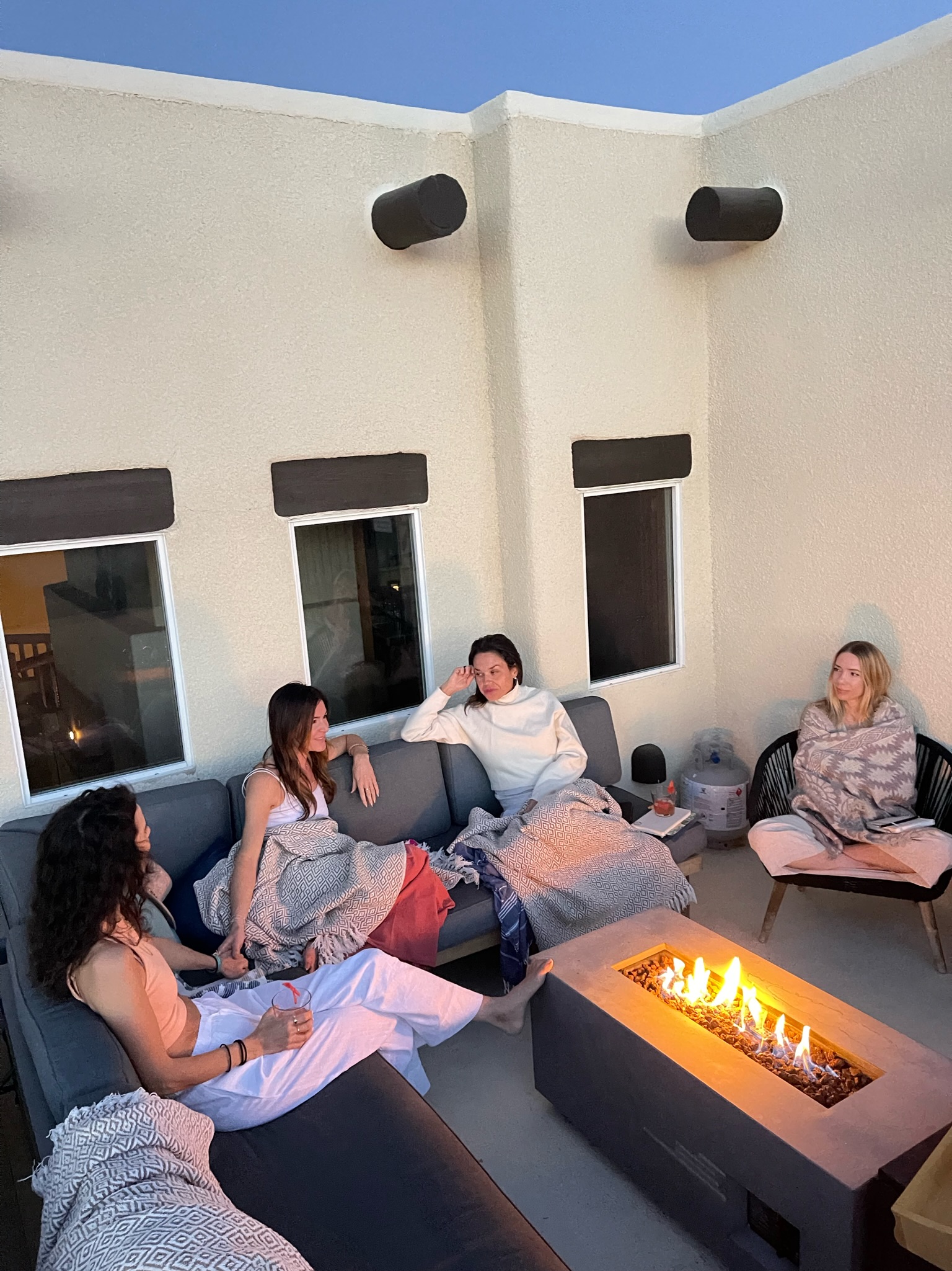 Women gathered around a fire pit on the rooftop patio at dusk